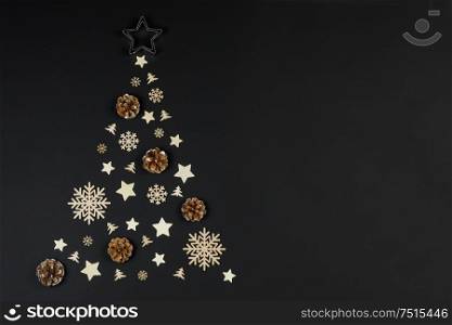 Christmas Tree made of wooden decor and pine cones on black paper background. Christmas Holiday Concept. Flat Lay. Christmas Holiday Concept