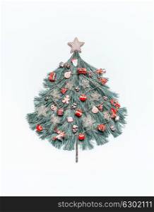 Christmas tree made with fir branches, decorated with star and red festive decorations , holidays cookies, gingerbread man and Santa on white background, top view. Festive layout for greeting card