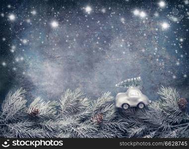 Christmas tree on toy car rides on fir branches on dar blue background with painted snow. Greeting card with copy space for your design