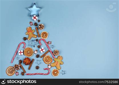 Christmas tree symbol composition. Ginger cookies caramel candy canes mold star form gifts orange and baubles, flat lay with copy space. Christmas tree symbol