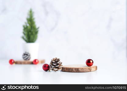 christmas tree with pine cone and decor xmas ball and empty wood log plate on white table and marble tile wall background.clean minimal simple style.holiday still life mockup to display design