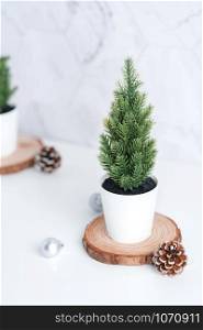 christmas tree with pine cone,decor xmas ball on wood log at white table and marble tile wall background.clean minimal simple style.holiday still life with space to adding text