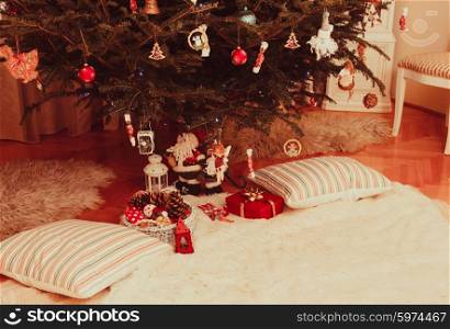 Christmas tree with presents underneath of Santa Claus and two pillows lying along. Christmas tree in living room