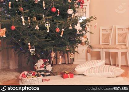 Christmas tree with presents underneath of Santa Claus and two pillows lying along. Christmas tree in living room
