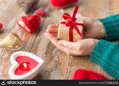 christmas, valentines day and holidays concept - close up of female hands holding gift box with heart shaped decorations and candle burning on wooden background. close up of hands holding christmas gift