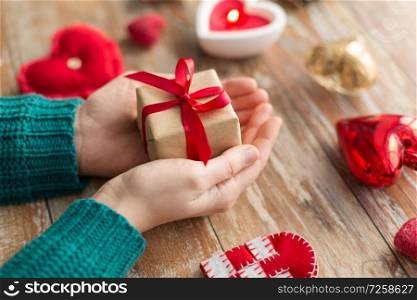 christmas, valentines day and holidays concept - close up of female hands holding gift box with heart shaped decorations on wooden background. close up of hands holding christmas gift