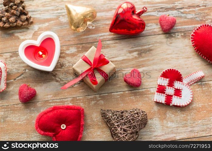 christmas, valentines day and holidays concept - gift box with heart shaped decorations and candle burning on wooden background. christmas gift, heart shaped decorations, candle
