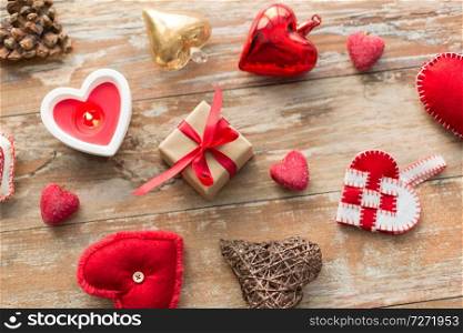 christmas, valentines day and holidays concept - gift box with heart shaped decorations and candle burning on wooden background. christmas gift, heart shaped decorations, candle