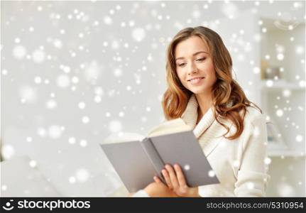 christmas, winter and people concept - happy young woman reading book at home over snow. happy young woman reading book at home