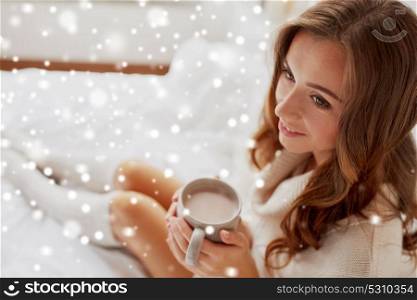 christmas, winter and people concept - happy young woman with cup of coffee or cocoa in bed at home over snow. happy woman with cup of cocoa in bed at home