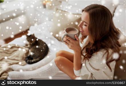 christmas, winter and people concept - happy young woman with cup of coffee or tea in bed at home bedroom over snow. happy woman with cup of coffee in bed at home