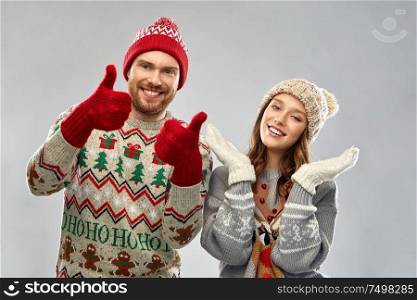 christmas, winter clothes and holidays concept - portrait of happy couple at ugly sweater party showing thumbs up. happy couple at christmas ugly sweater party