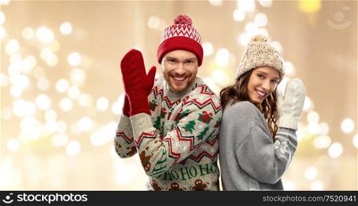 christmas, winter clothes and holidays concept - portrait of happy couple at ugly sweater party over festive lights background. happy couple at christmas ugly sweater party