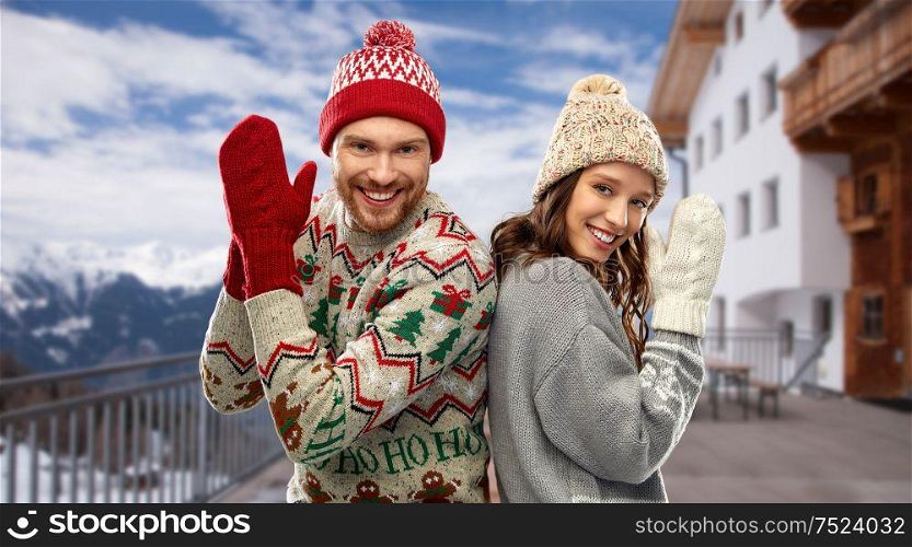 christmas, winter clothes and holidays concept - portrait of happy couple in ugly sweaters over ski resort background. happy couple in ugly christmas sweaters in winter