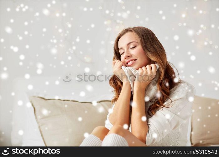 christmas, winter, comfort and people concept - happy young woman in warm pullover at home over snow. happy young woman in warm pullover at home