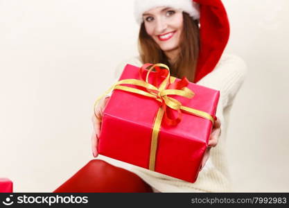 Christmas winter happiness concept. Smiling latin woman wearing santa helper hat holding present red gift box