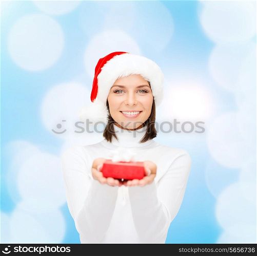 christmas, winter, happiness, holidays and people concept - smiling woman in santa helper hat with small red gift box over blue lights background