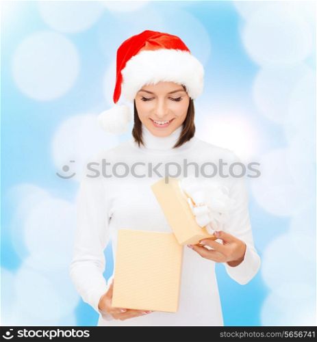 christmas, winter, happiness, holidays and people concept - smiling woman in santa helper hat opening gift box over blue lights background