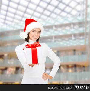christmas, winter, happiness, holidays and people concept - smiling woman in santa helper hat with gift box over shopping center background