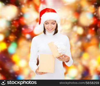 christmas, winter, happiness, holidays and people concept - smiling woman in santa helper hat opening gift box over red lights background