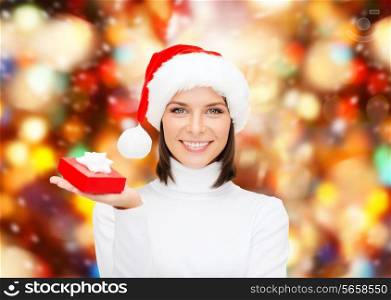 christmas, winter, happiness, holidays and people concept - smiling woman in santa helper hat with small red gift box over lights background