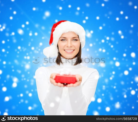 christmas, winter, happiness, holidays and people concept - smiling woman in santa helper hat with small red gift box over blue snowy background