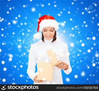 christmas, winter, happiness, holidays and people concept - smiling woman in santa helper hat opening gift box over blue snowy background