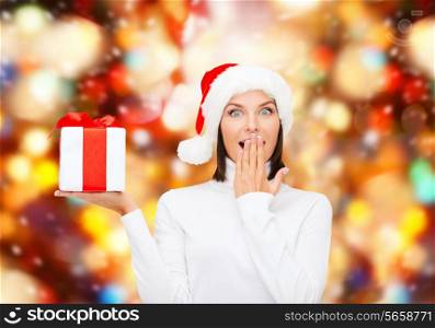 christmas, winter, happiness, holidays and people concept - smiling woman in santa helper hat with gift box over red lights background