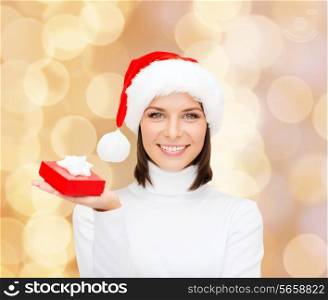 christmas, winter, happiness, holidays and people concept - smiling woman in santa helper hat with small red gift box over beige lights background