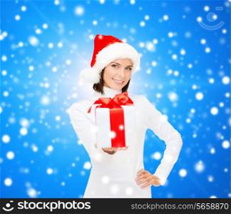 christmas, winter, happiness, holidays and people concept - smiling woman in santa helper hat with gift box over blue snowy background