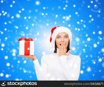 christmas, winter, happiness, holidays and people concept - smiling woman in santa helper hat with gift box over blue snowy background