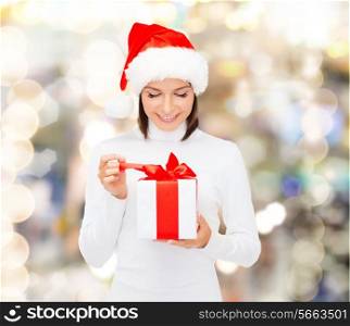 christmas, winter, happiness, holidays and people concept - smiling woman in santa helper hat with gift box over lights background