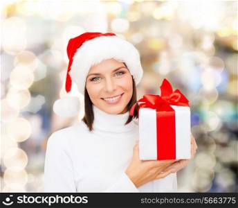 christmas, winter, happiness, holidays and people concept - smiling woman in santa helper hat with gift box over lights background