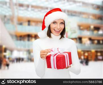 christmas, winter, happiness, holidays and people concept - smiling woman in santa helper hat with gift box over shopping center background