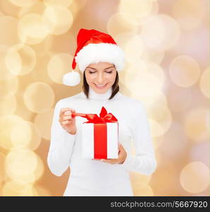 christmas, winter, happiness, holidays and people concept - smiling woman in santa helper hat with gift box over beige lights background