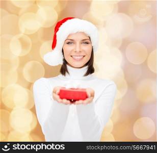 christmas, winter, happiness, holidays and people concept - smiling woman in santa helper hat with small red gift box over beige lights background