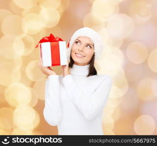 christmas, winter, happiness, holidays and people concept - smiling woman in santa helper hat with gift box over beige lights background