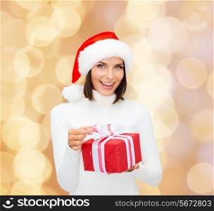 christmas, winter, happiness, holidays and people concept - smiling woman in santa helper hat with gift box over beige lights background