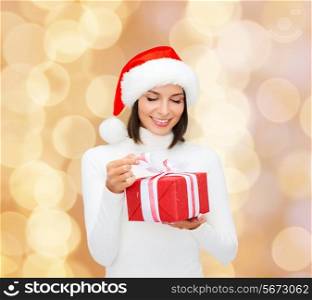 christmas, winter, happiness, holidays and people concept - smiling woman in santa helper hat with gift box over beige lights background