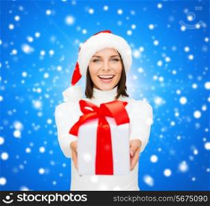 christmas, winter, happiness, holidays and people concept - smiling woman in santa helper hat with gift box over blue snowy background