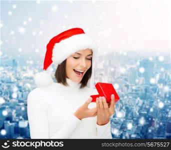 christmas, winter, happiness, holidays and people concept - smiling woman in santa helper hat with gift box over snowy city background