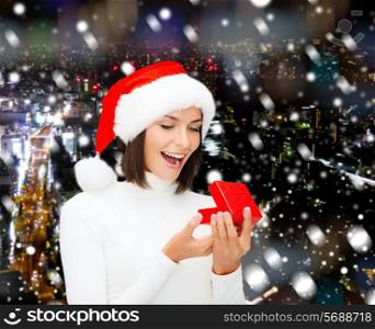 christmas, winter, happiness, holidays and people concept - smiling woman in santa helper hat with gift box over snowy night city background