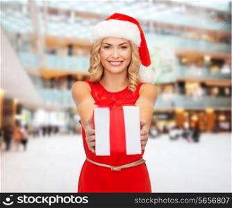 christmas, winter, happiness, holidays and people concept- smiling woman in santa helper hat with gift box over shopping center background