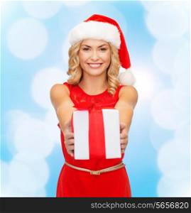 christmas, winter, happiness, holidays and people concept- smiling woman in santa helper hat with gift box over blue lights background