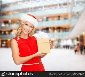 christmas, winter, happiness, holidays and people concept- smiling woman in santa helper hat with gift box over shopping center background