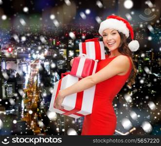 christmas, winter, happiness, holidays and people concept- smiling woman in santa helper hat with gift boxes over snowy night city background
