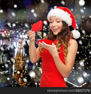 christmas, winter, happiness, holidays and people concept- smiling woman in santa helper hat with gift box over snowy night city background