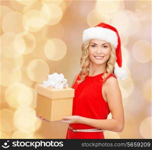 christmas, winter, happiness, holidays and people concept- smiling woman in santa helper hat with gift box over beige lights background
