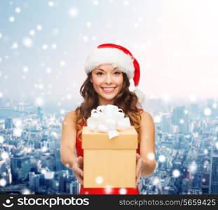 christmas, winter, happiness, holidays and people concept- smiling woman in santa helper hat with gift box over snowy night city background
