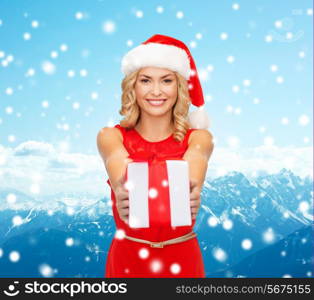 christmas, winter, happiness, holidays and people concept- smiling woman in santa helper hat with gift box over blue snowy mountains background